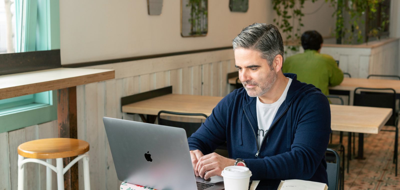 A man working on a laptop in a café with notes and coffee, symbolizing focus and analysis involved in a technical SEO audit.