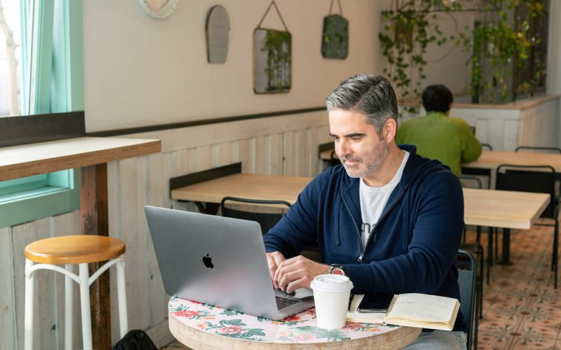 A man working on a laptop in a café with notes and coffee, symbolizing focus and analysis involved in a technical SEO audit.
